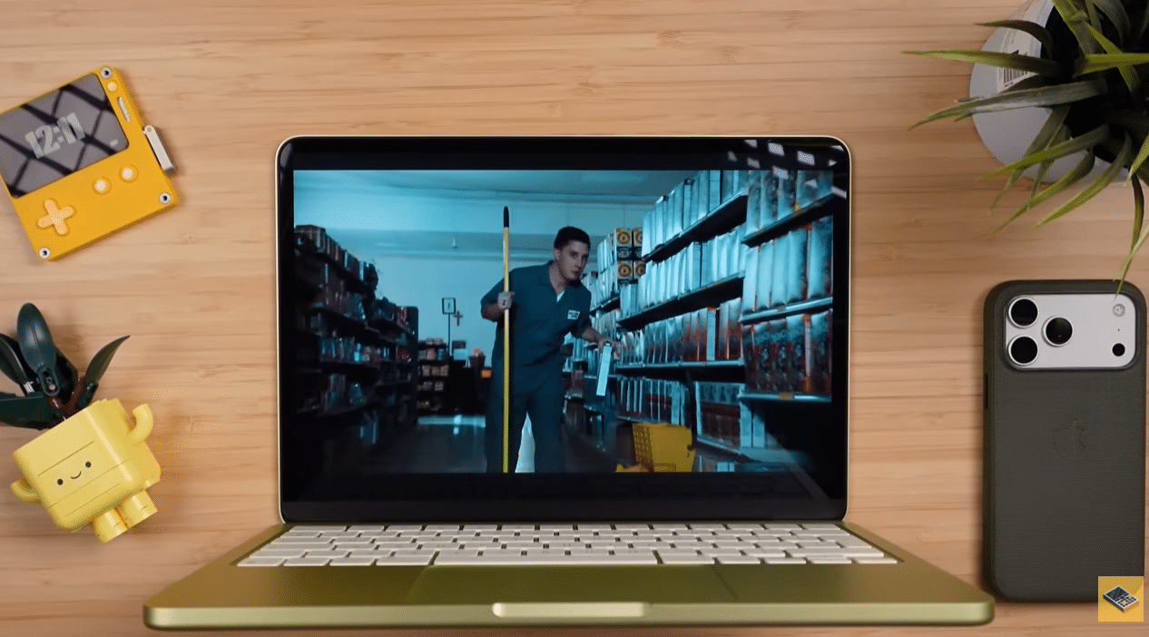 MacBook Neo лимонного кольору відтворює відео на екрані, розміщений на дерев'яному столі