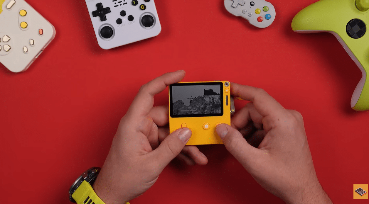 Жовта консоль PlayDate в руках на червоному тлі поруч з іншими геймпадами; на чорно-білому екрані відображається гра
