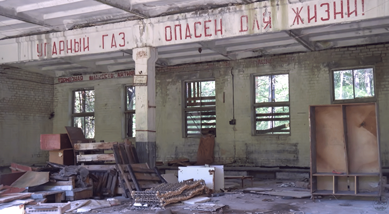 Занедбаний гараж у Чорнобилі-2 з радянським написом «Угарний газ опасен для жизни» на стіні та розкиданим сміттям на підлозі
