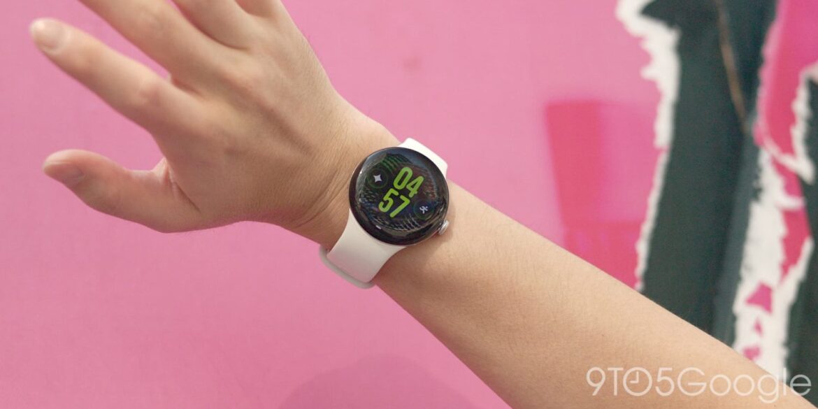 Смарт-годинник Google Pixel Watch зі світлим ремінцем на руці людини на рожевому тлі, дисплей показує час та показники
