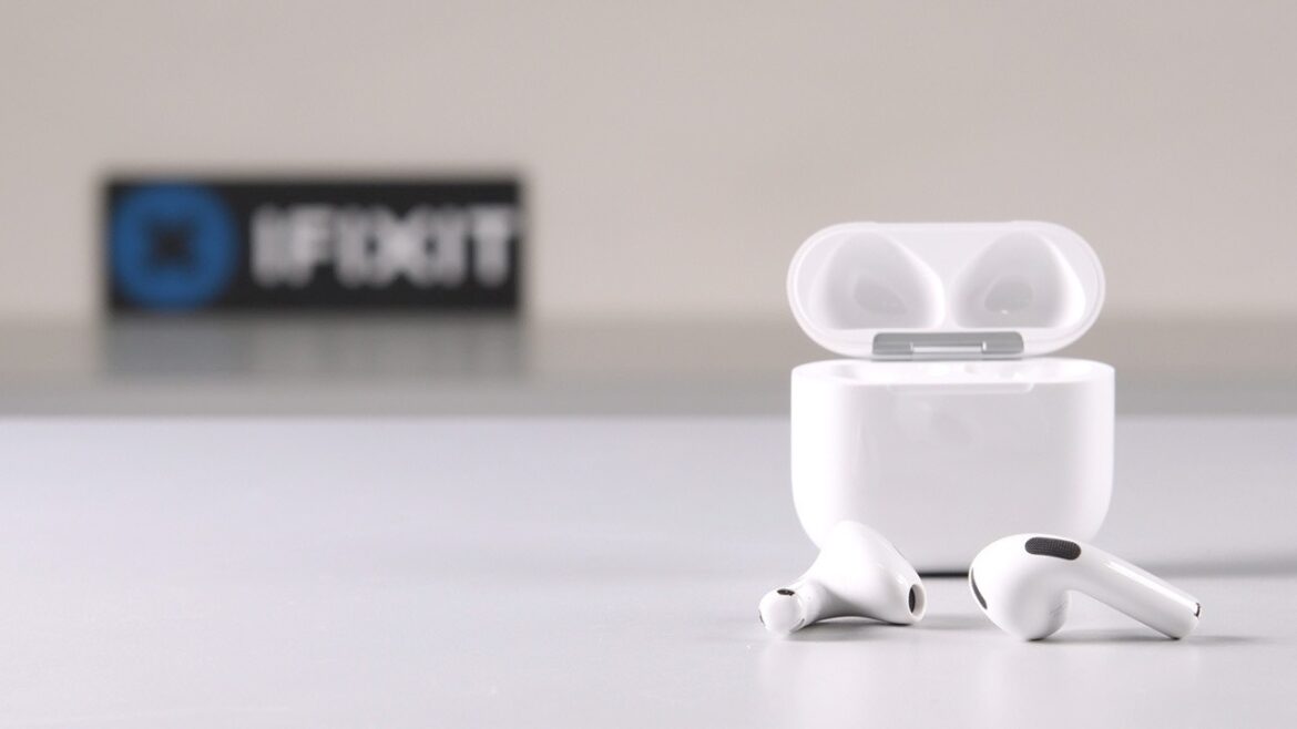 AirPods 5 з відкритим кейсом та двома навушниками поруч, на фоні логотипу iFixit