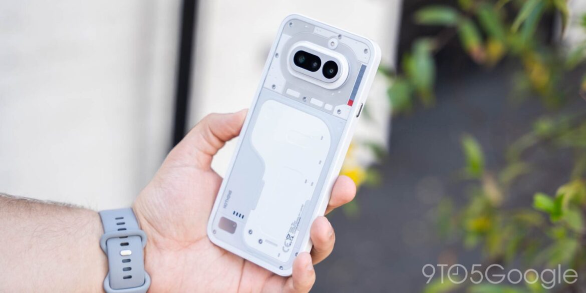Рука тримає смартфон Nothing Phone (4a) з прозорою задньою панеллю, показуючи внутрішню конструкцію пристрою на тлі зелені