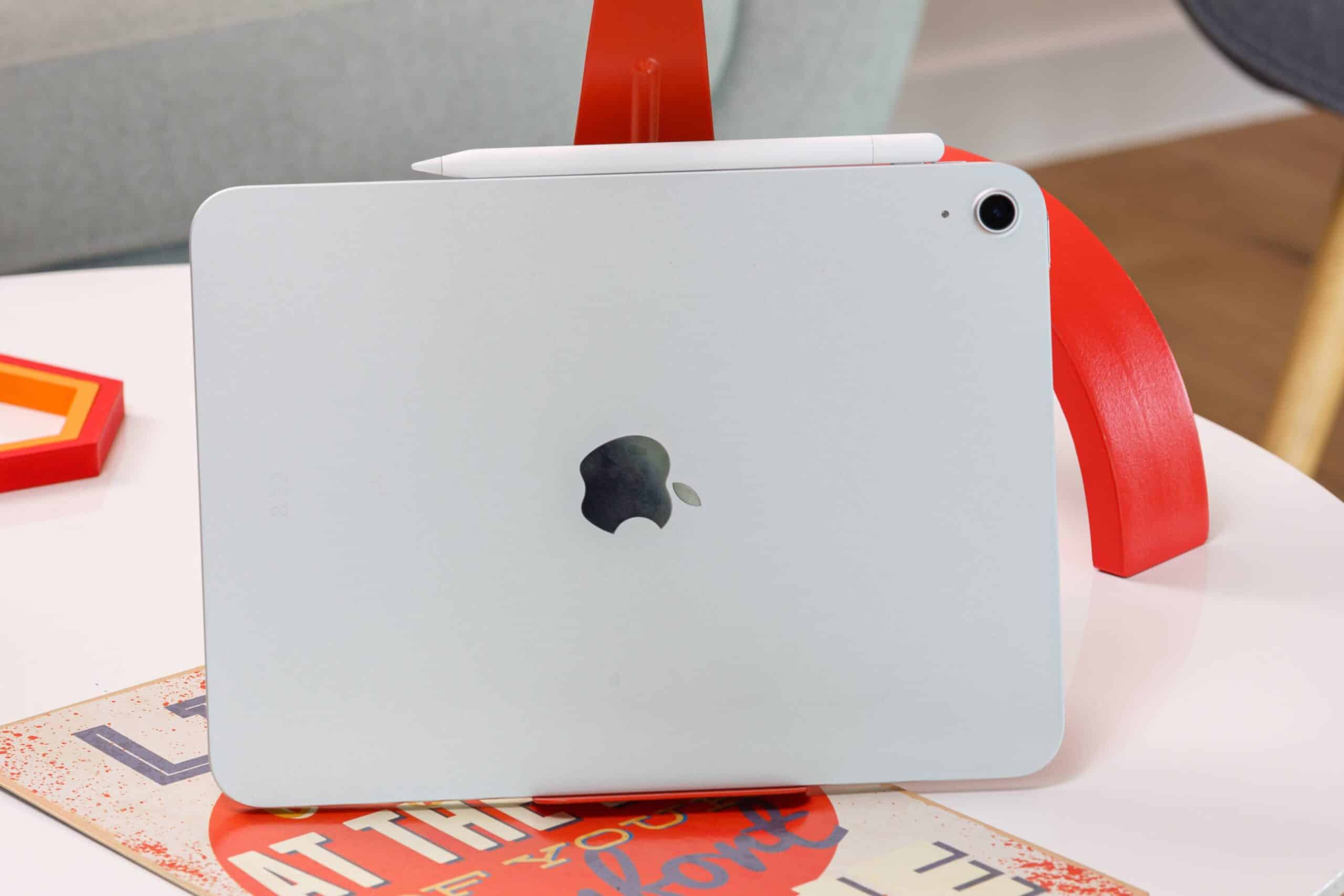 Білий iPad з логотипом Apple лежить на столі рядом з червоною підставкою та стилусом Apple Pencil