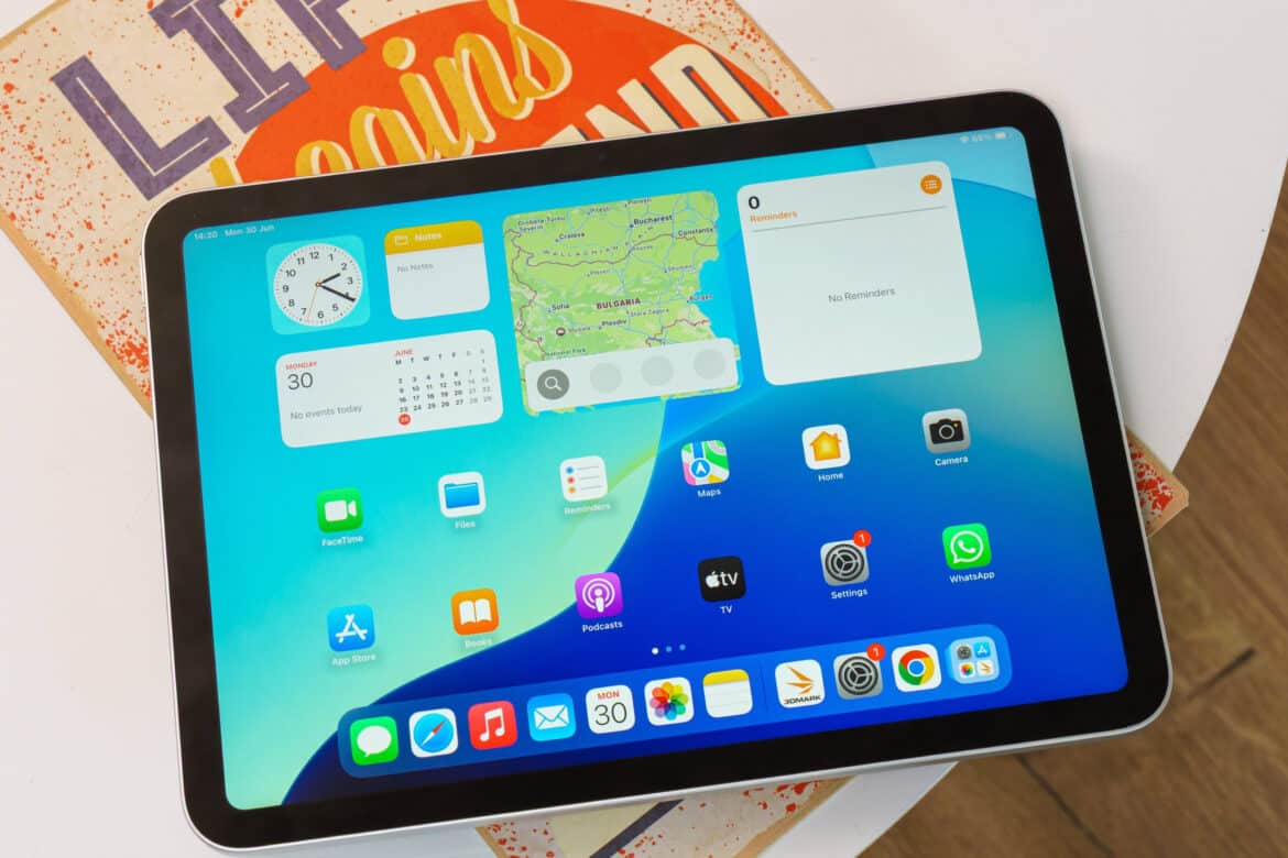 IPad із чорною рамкою на екрані якого видно голубий фон з віджетами та іконками додатків, включаючи App Store та інші