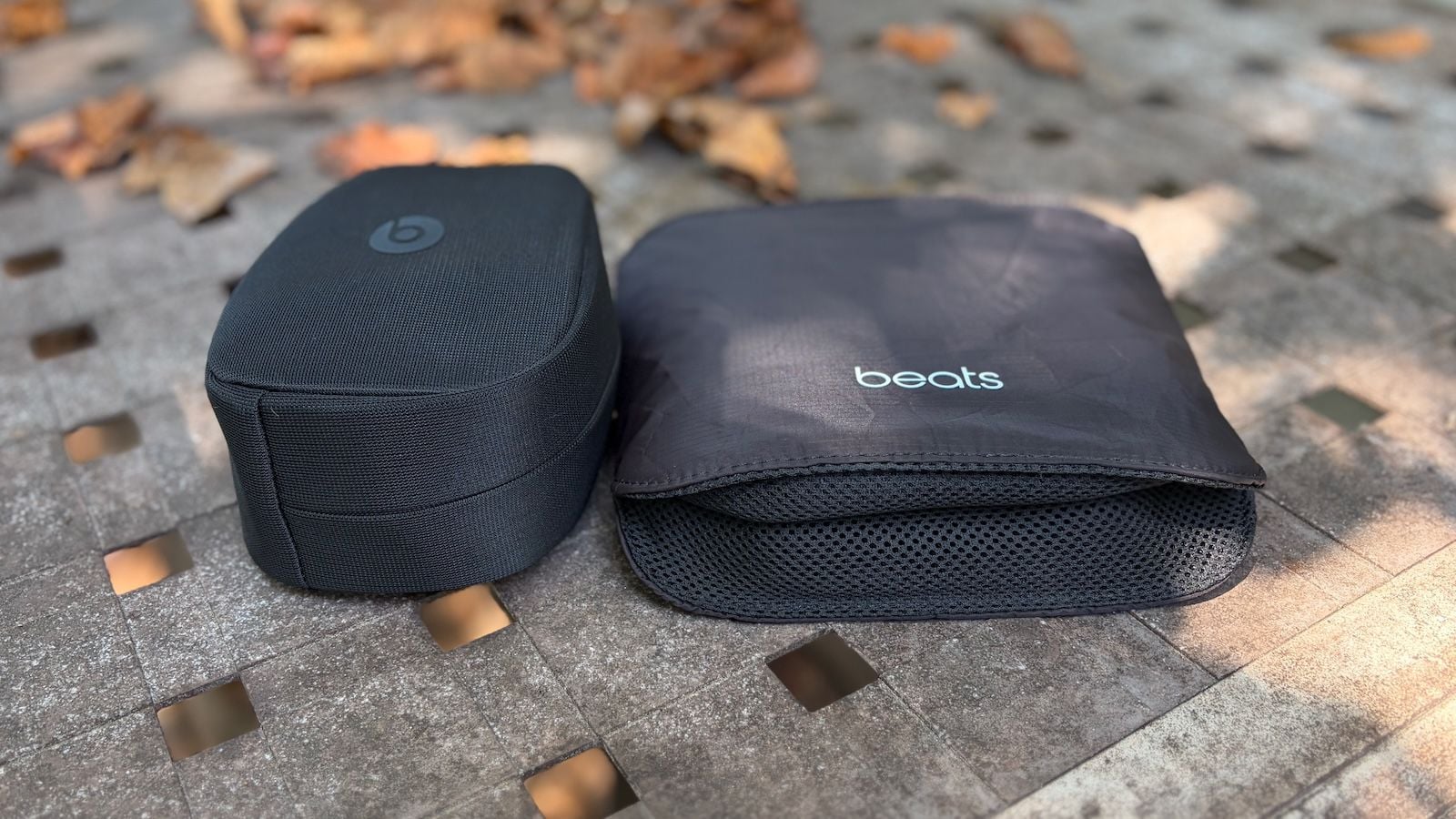 Два чорні чохли для навушників Beats 360 - жорсткий та м'який - розташовані поруч на брусчатці