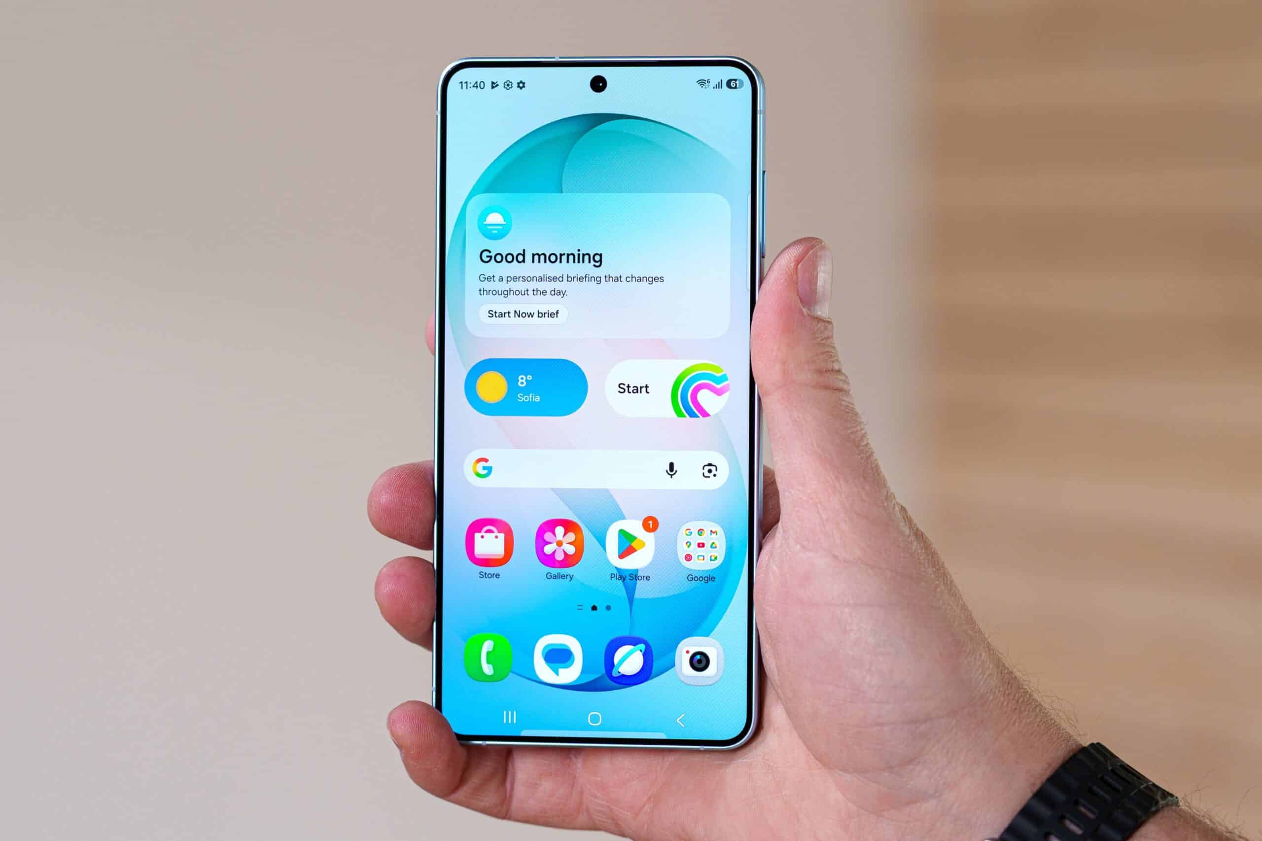 Рука тримає один смартфон Samsung Galaxy з увімкненим дисплеєм, що показує домашній екран з іконками застосунків і