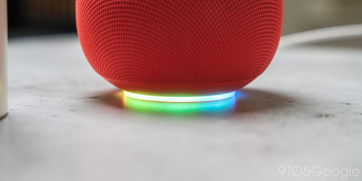 Червона розумна колонка Google Home з підсвітленою основою зеленого та синього кольору, розташована на сірій поверхні