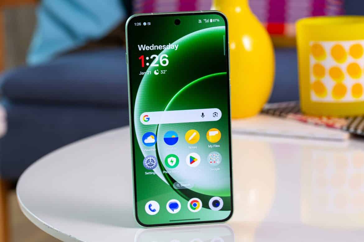 OnePlus Ace 7 на білому столі поруч з жовтою чашкою, екран показує аналогічний інтерфейс з часом і додатками