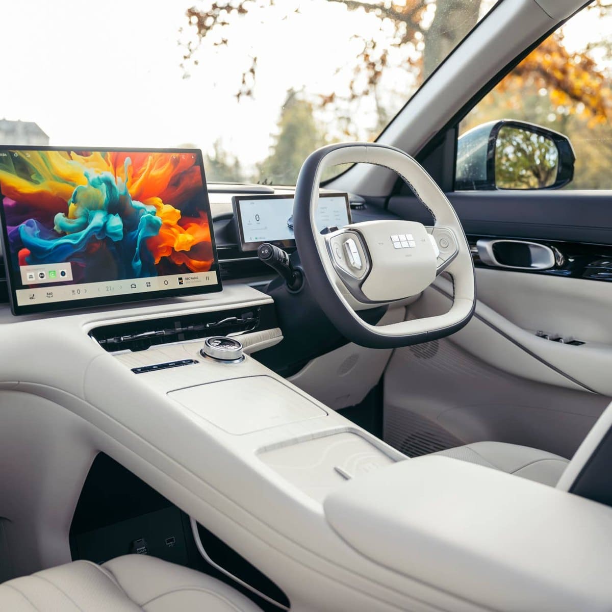 Світлий салон Geely з великим екраном на торпедо, білим кермом і бежевими шкіряними сидіннями