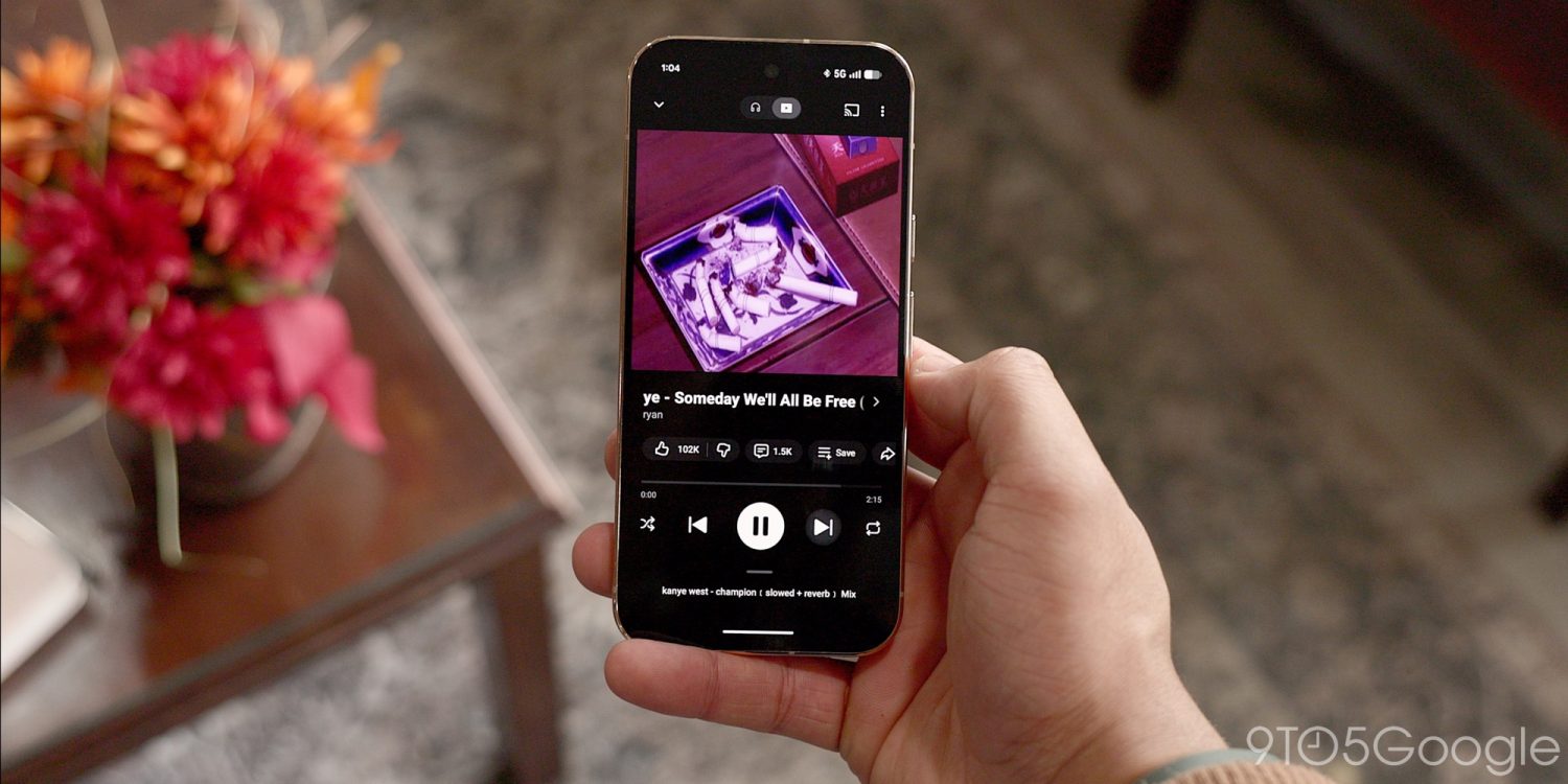 Смартфон у руці з екраном YouTube Music, де відтворюється трек з фіолетовою обкладинкою
