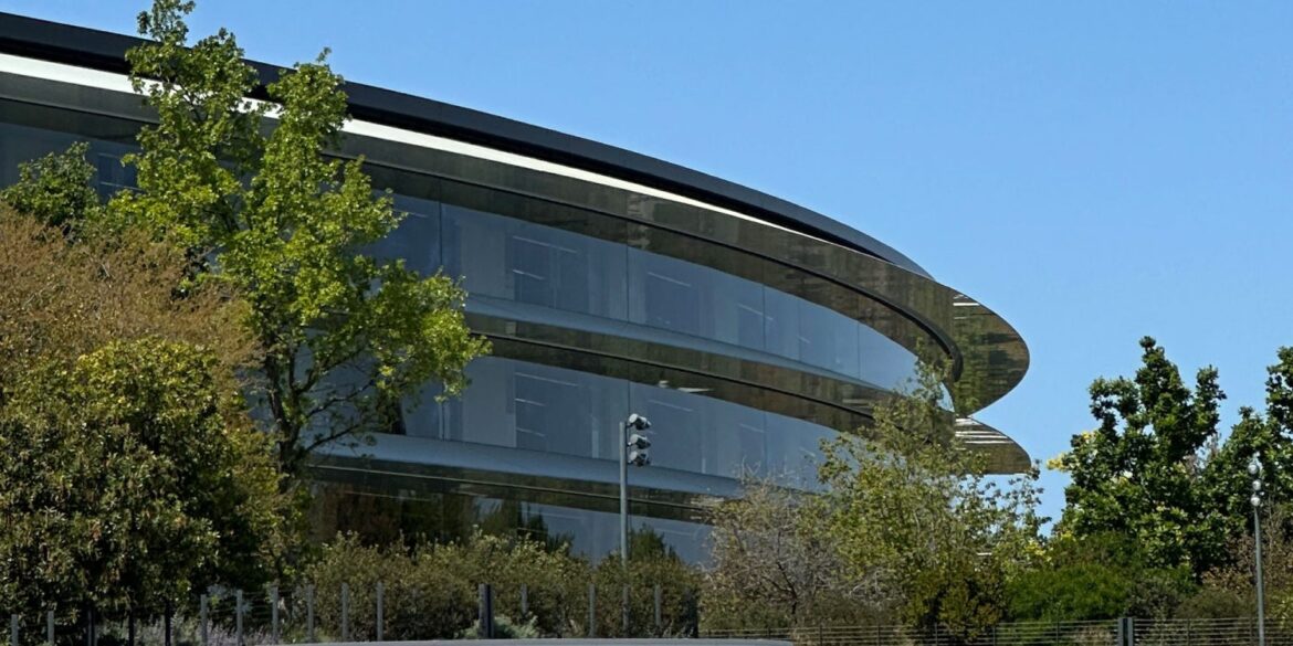 Сучасна будівля Apple Park з криволінійною архітектурою та панорамними вікнами серед зелених дерев
