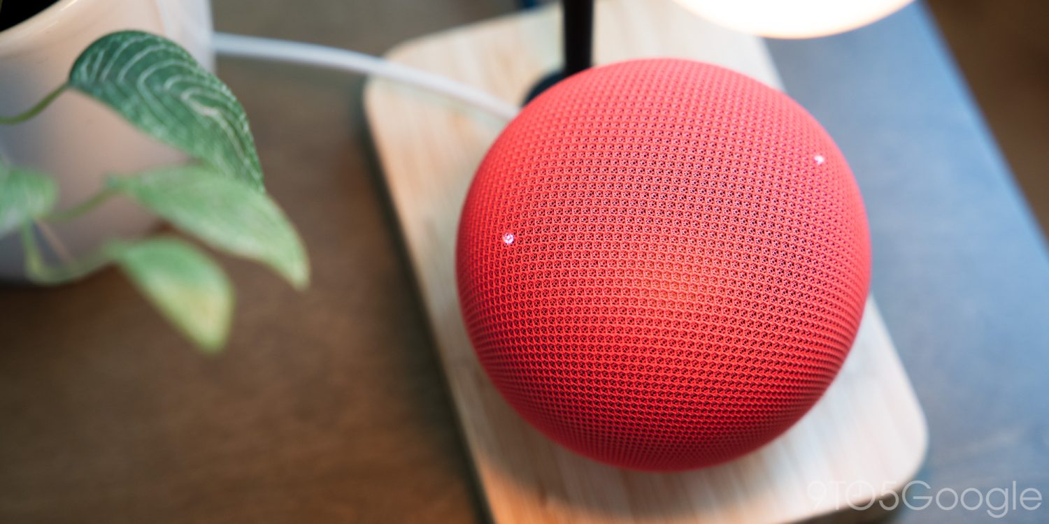 Червоний голосовий динамік Google Home на білій підставці поруч із кімнатною рослиною