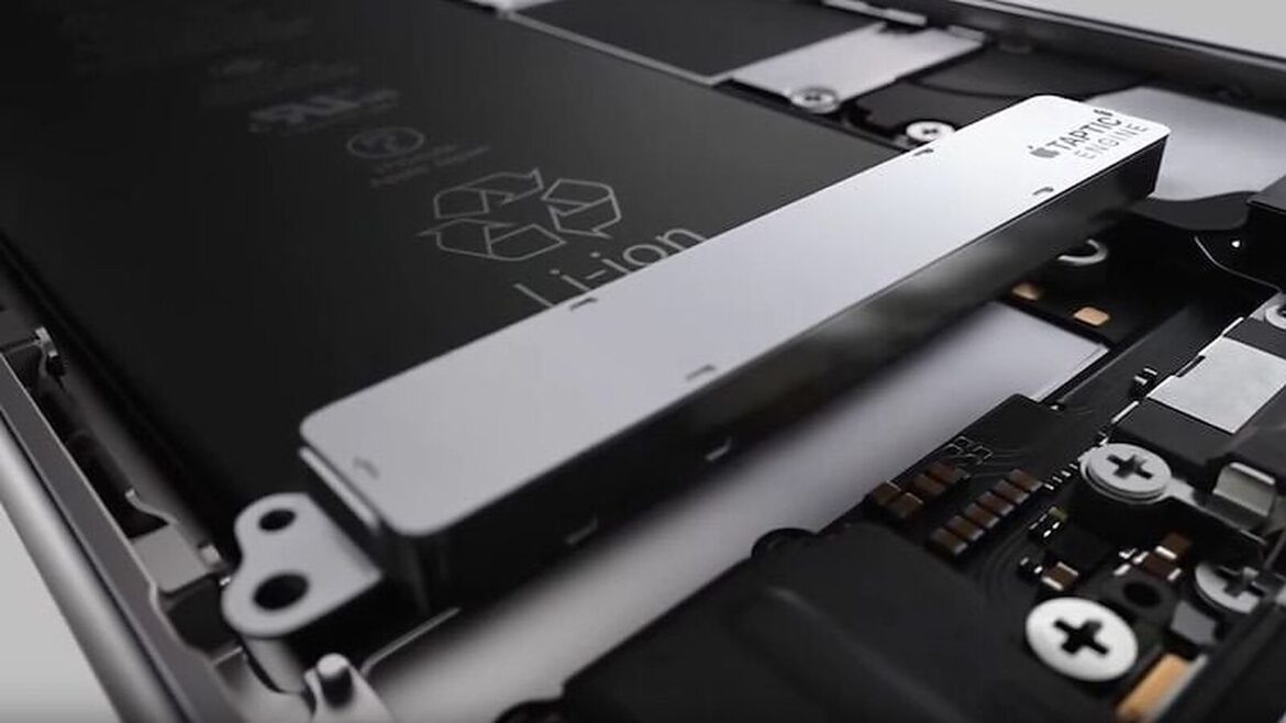 Крупний план розібраного смартфона: срібляста вібромодуль Taptic Engine лежить на акумуляторі Li-ion поруч із гвинтами і