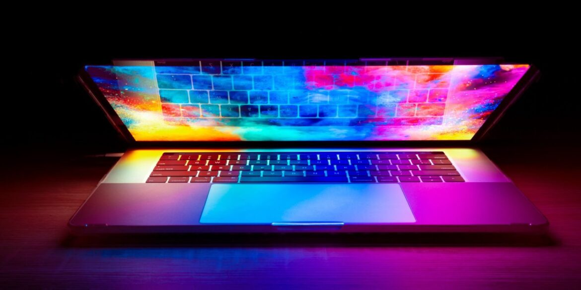 Відкритий MacBook Pro з кольоровим дисплеєм на чорному тлі, освітлений неоновим світлом у відтінках синього, рожевого та