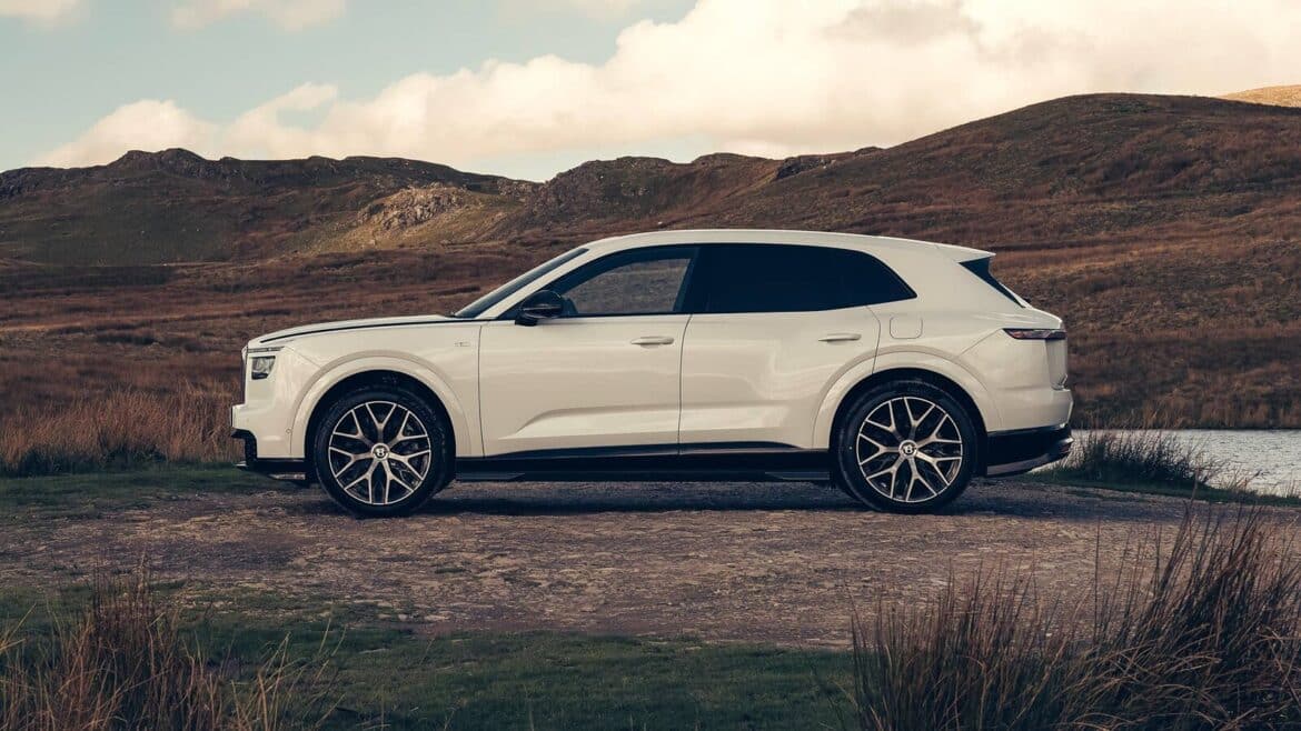 Білий електричний позашляховик Bentley Torcal у профіль на гравійній стоянці біля озера на тлі коричневих пагорбів