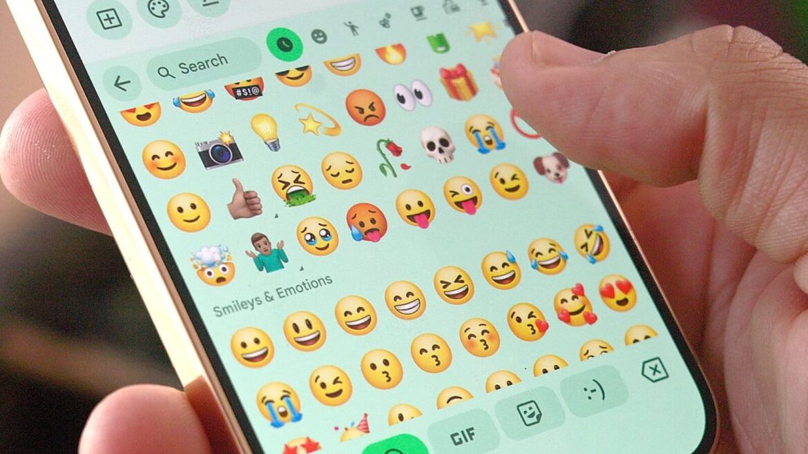 Рука тримає смартфон з клавіатурою емодзі у розділі «Smileys & Emotions» з округлими яскравими смайликами