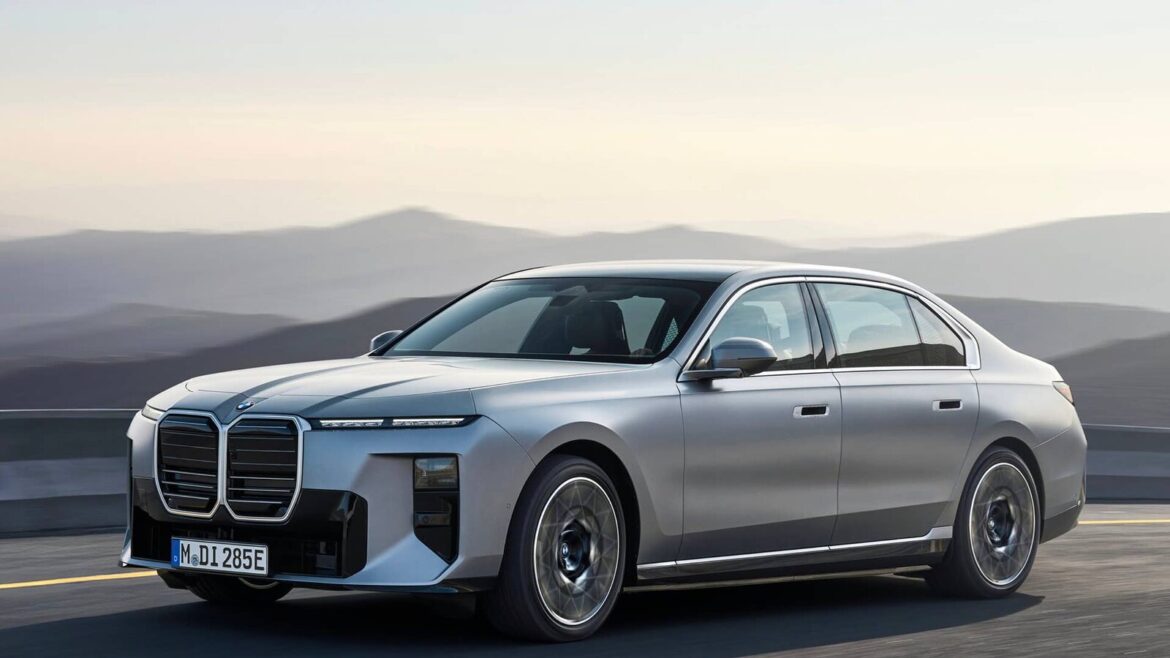 Срібний електромобіль BMW i7 з великими решітками радіатора їде асфальтованою дорогою на тлі гірського пейзажу на заході