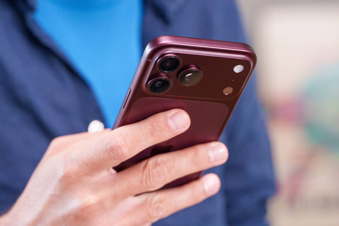Людина в синій одежі тримає в руці бордовий смартфон iPhone з потрійною камерою на задній панелі