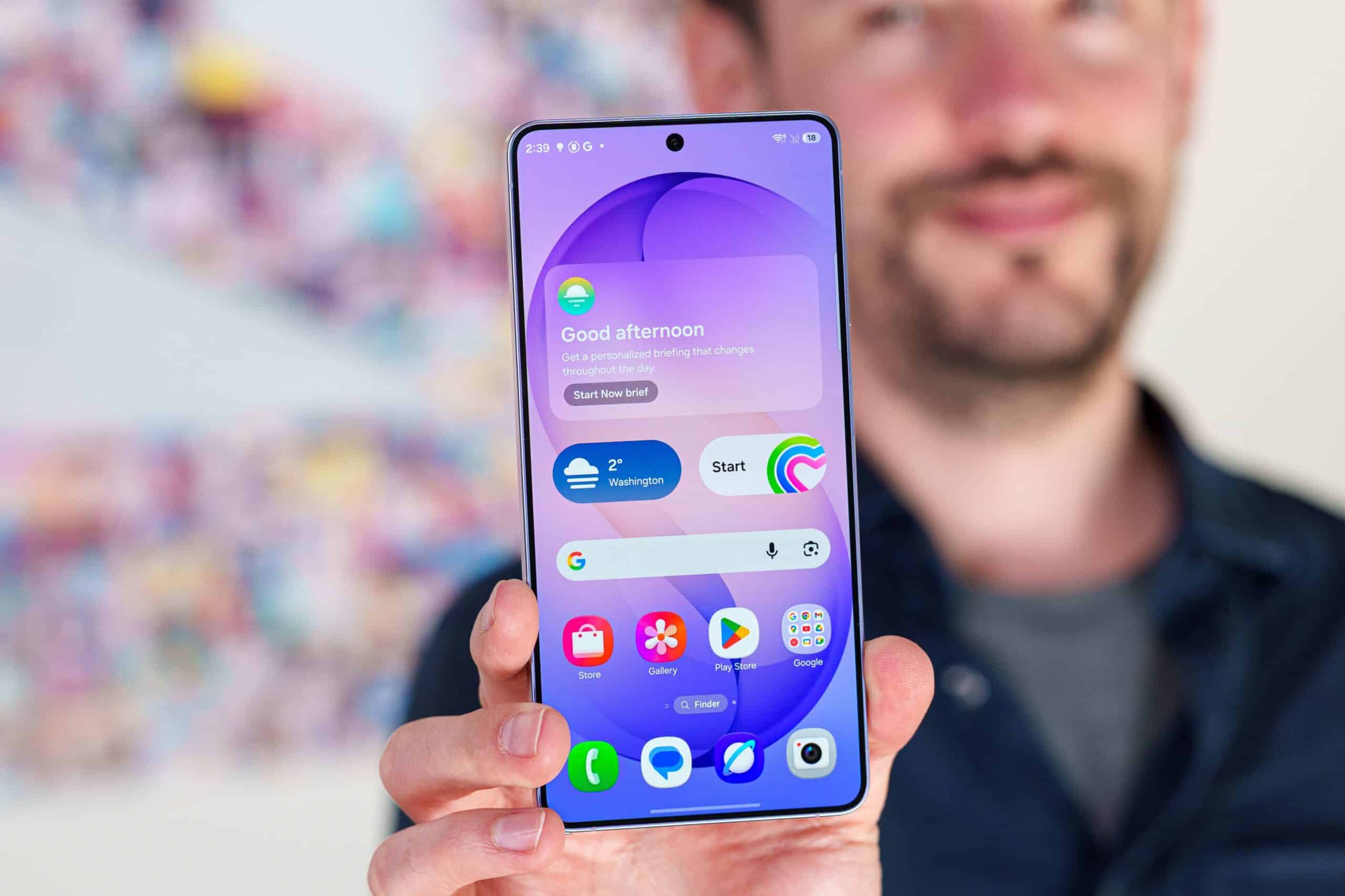 Чоловік демонструє смартфон Samsung з фіолетовим домашнім екраном та віджетами