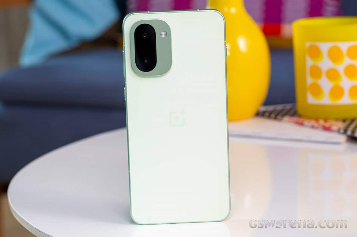 OnePlus 16R білого кольору зі стороною камер, розташований на столі на фоні жовтих предметів