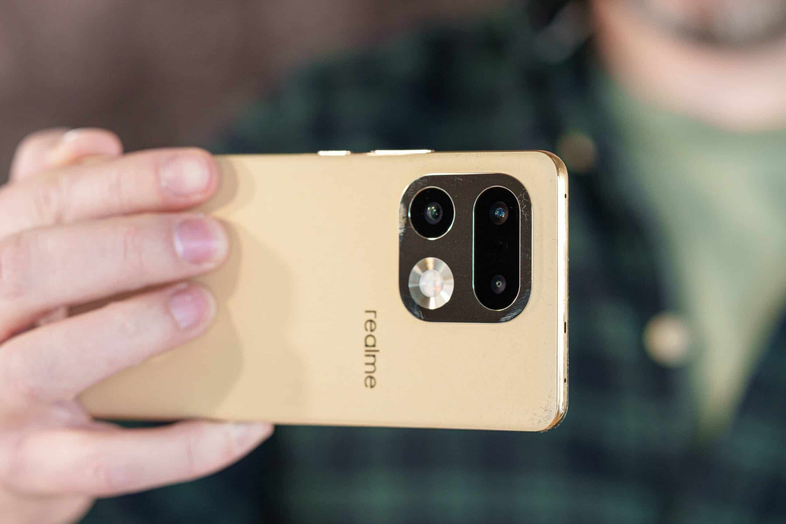 Смартфон Realme золотистого кольору з потрійною камерою та металевою рамкою в руці