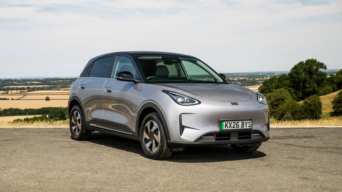 Срібляста електрична Geely з британським номерним знаком на тлі сільської місцевості з полями та деревами