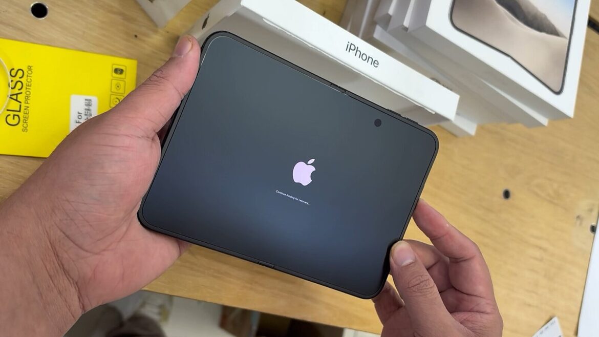 Руки тримають розпакований пристрій із логотипом Apple на екрані, поруч коробки з написом iPhone на столі