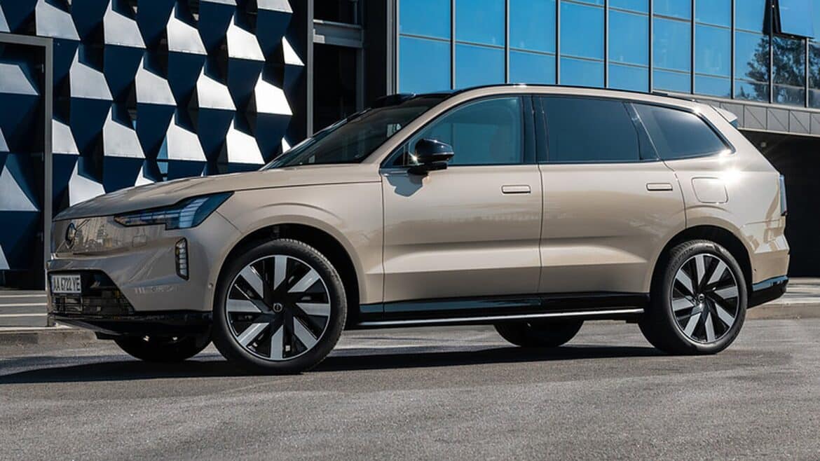 Бежевий позашляховик Volvo стоїть на асфальті перед будівлею з геометричним синім фасадом