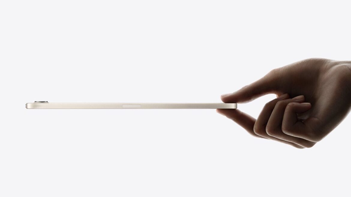 Планшет iPad mini збоку, затиснутий двома пальцями руки на світлому фоні