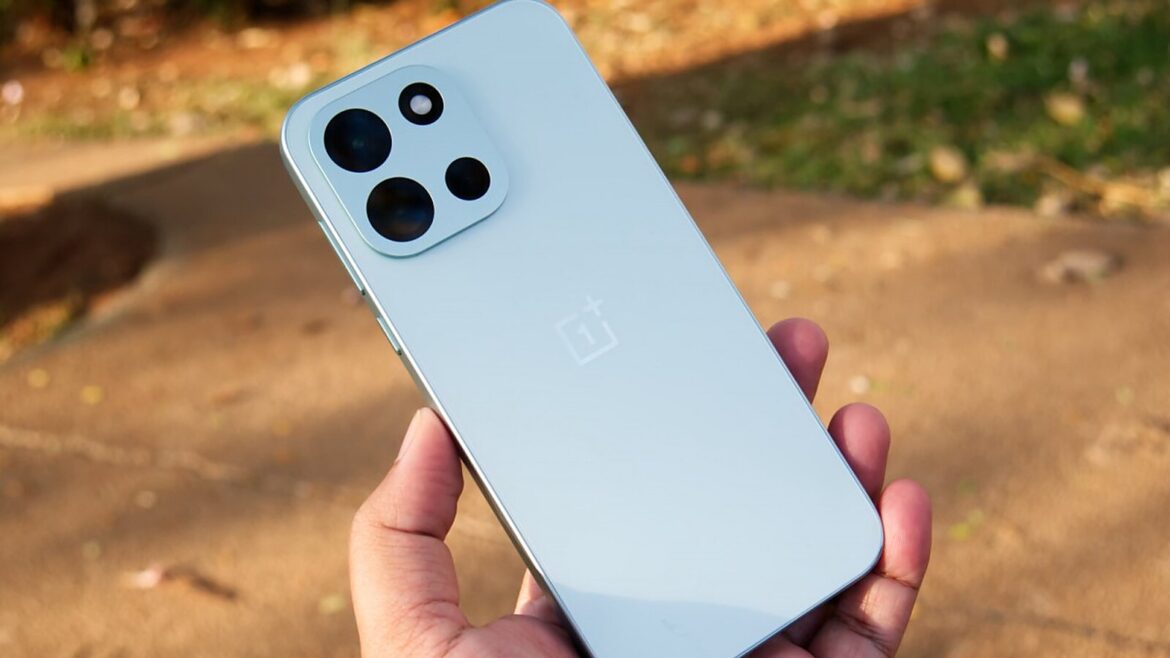 Рука тримає блакитний смартфон OnePlus із квадратним блоком камер на задній панелі на тлі розмитої доріжки